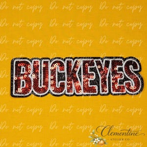May include: A decorative patch featuring the word BUCKEYES in bold, block letters. The letters are filled with shiny red sequins and outlined in a thick black border with a thin white inner trim, set against a solid mustard yellow background.