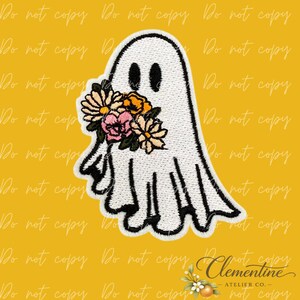 Puede incluir: Un parche bordado que muestra un personaje fantasma blanco con ojos ovalados negros. El fantasma sostiene un grupo de flores en tonos amarillo, naranja, rosa y verde. El parche tiene un borde negro grueso bordado sobre un fondo amarillo.