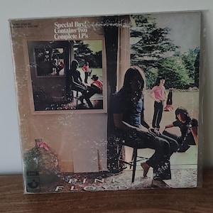 Könnte beinhalten: Vintage Pink Floyd Albumcover mit Bandmitgliedern in einer natürlichen Umgebung. Das Albumcover trägt den Text "Special Buy! Contains Two Complete LP's". Das Album befindet sich in einer Plastikhülle.