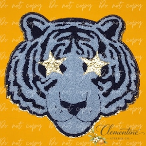 May include: A tiger head patch featuring a light blue and dark navy blue textured design. The tiger has two gold glitter stars positioned over its eyes and a gold glitter border outlining the entire shape of the animal head.