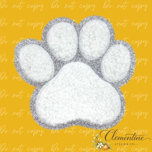 May include: A paw print patch featuring a white, textured, sherpa-like material for the pads and toes, outlined with a shimmering silver glitter border. The design is set against a solid mustard yellow background with a repeating watermark.