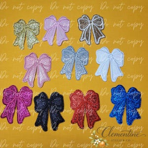 May include: A collection of eleven embroidered bow patches in various colours including gold, lavender, brown, pink, silver, light blue, magenta, dark blue, red, and royal blue, each featuring a textured glitter finish and stitched edges.