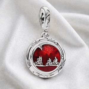 Peut inclure: Pendentif de charme argenté avec un centre rond en émail rouge représentant trois cyclistes sur fond étoilé. Le charme a une bordure décorative et une boucle pour l'attacher à un bracelet ou un collier.