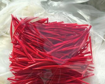 Op de afbeelding: Een doorzichtig plastic zakje gevuld met een grote hoeveelheid dunne, felrode veerschachten. De individuele schachten zijn recht, slank en uniform van kleur, en zitten strak verpakt in het rechthoekige zakje.