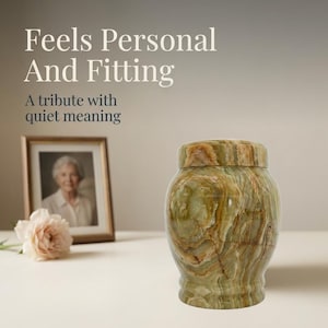May include: A polished green onyx stone urn with a rounded body and a matching lid. The text "Feels Personal And Fitting" and "A tribute with quiet meaning" is visible in the upper left corner, alongside a framed photograph and a pale pink flower.