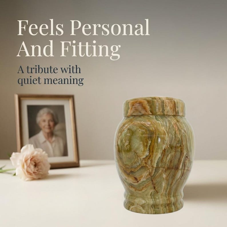 May include: A polished green onyx stone urn with a rounded body and a matching lid. The text "Feels Personal And Fitting" and "A tribute with quiet meaning" is visible in the upper left corner, alongside a framed photograph and a pale pink flower.