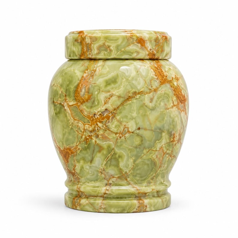 May include: A cylindrical urn crafted from polished green onyx stone, featuring a smooth, rounded body with a distinct base and a matching removable lid. The surface displays a natural, marbled pattern of light green, sage, and deep amber veins.