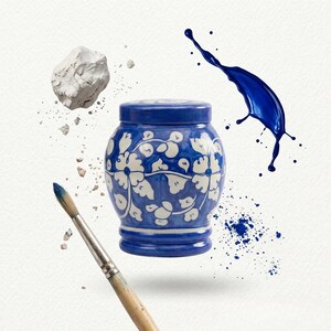 May include: A blue and white ceramic jar with a lid, featuring a hand-painted floral pattern. The jar is surrounded by a wooden paintbrush, a white rock fragment, and a dynamic splash of blue paint against a plain white background.