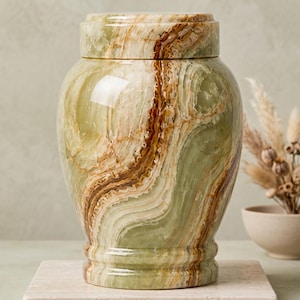 Handcrafted light green onyx cremation urn displayed on a sunlit wooden windowsill beside a white orchid and glass candle, with warm natural light and a peaceful garden view in the background.