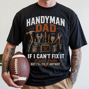 May include: Black t-shirt with the text "HANDYMAN DAD" and a tool belt graphic. The text "IF I CAN'T FIX IT, it ain't broke, BUT I'LL FIX IT ANYWAY" is also printed on the shirt. A brown football is held in the person's hand.