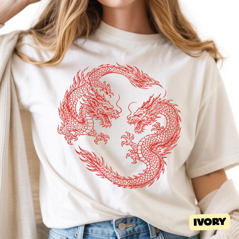 May include: An ivory short-sleeved t-shirt featuring a circular graphic of two red dragons facing each other in a mirrored pose. The dragons have detailed scales, flowing manes, and sharp claws. The word IVORY is printed in a small black box at the bottom.