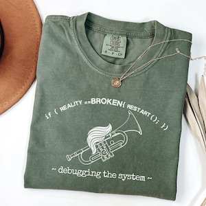 Pode incluir: Camiseta verde-oliva com o texto "if ( REALITY == BROKEN { RESTART (); } ) ~ debugging the system ~" e um gráfico branco de um instrumento musical. Um colar de ouro com um pingente está na camiseta.