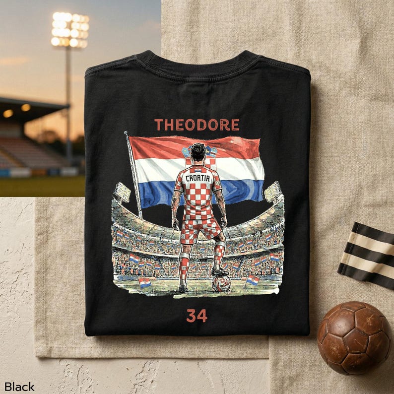 A black T-shirt with a graphic design depicting a soccer player standing in front of a stadium, with a flag of Croatia in the background.