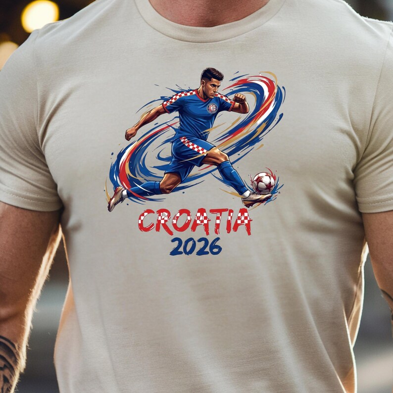 A person wearing a white t-shirt with a graphic design depicting a soccer player in a blue uniform kicking a soccer ball, with the text "CROATIA 2026" below the image.