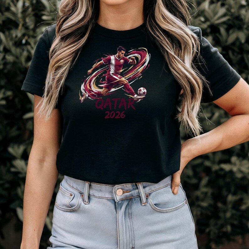 A woman wearing a black t-shirt with a graphic of a soccer player and the text "QATAR 2026" printed on it.