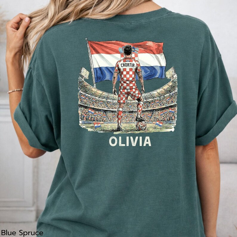 A green t-shirt with a graphic design depicting a person in a checkered outfit standing in front of a stadium, holding a flag.