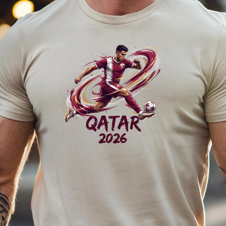 A person wearing a white t-shirt with a graphic design depicting a soccer player in a red uniform kicking a soccer ball.