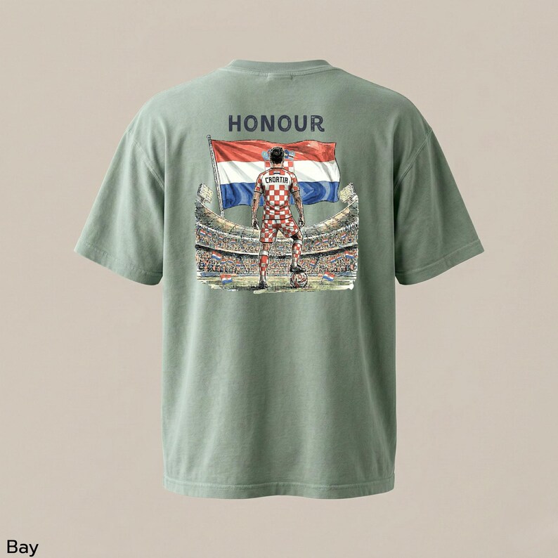 A green t-shirt with a graphic design on the back, depicting a person standing in front of a soccer stadium with a flag.