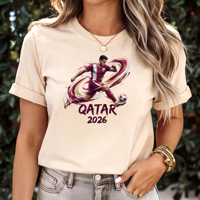 A woman wearing a white t-shirt with a graphic of a soccer player and the text "Qatar 2026" printed on it.
