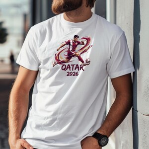 A man wearing a white t-shirt with a graphic of a soccer player and the text "QATAR 2026" printed on it.
