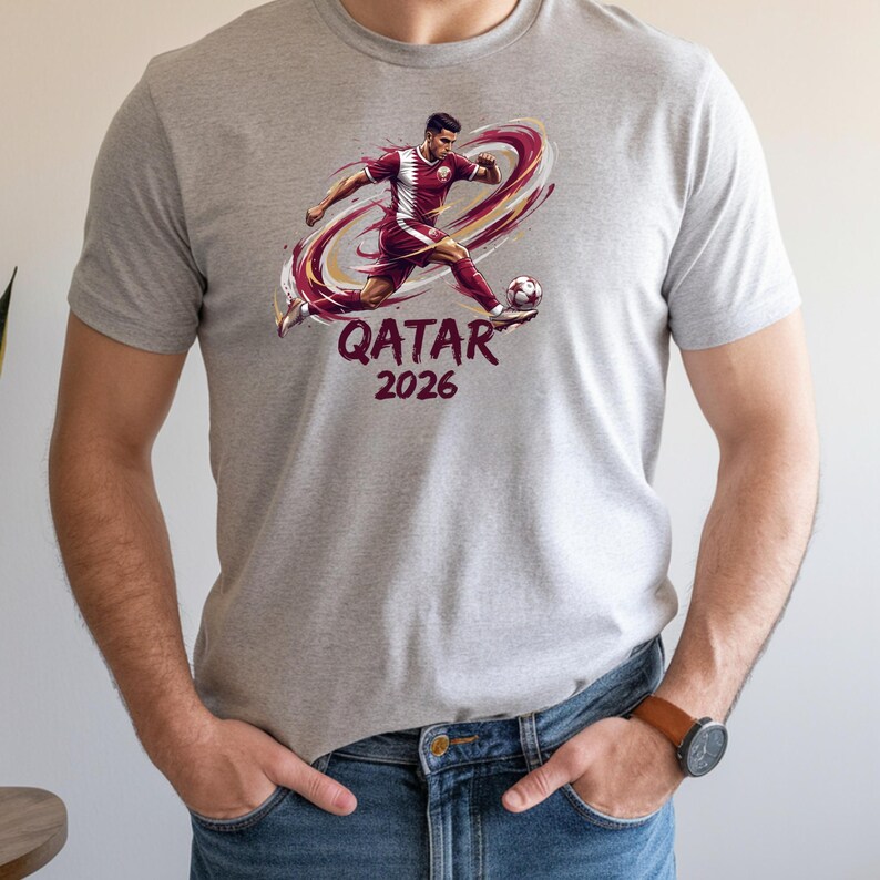 A man wearing a grey t-shirt with a graphic of a soccer player and the text "Qatar 2026" printed on it.