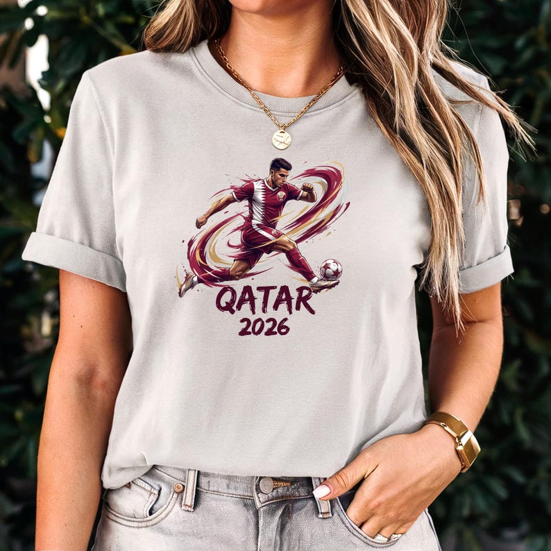 A woman wearing a white t-shirt with a graphic of a soccer player and the text "Qatar 2026" printed on it.