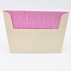 May include: A pink card with a textured surface is inside a beige envelope with a textured surface.