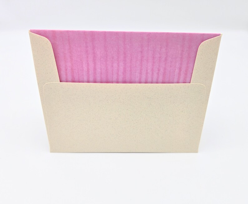 May include: A pink card with a textured surface is inside a beige envelope with a textured surface.