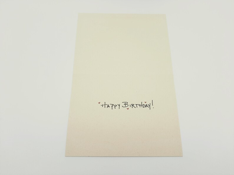 May include: A blank white card with the text "Happy Birthday!" written in black ink. There are small red hearts around the text.
