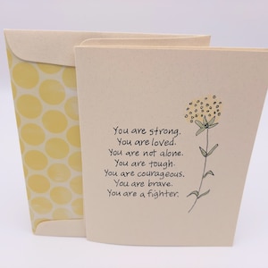 May include: A beige card with a yellow flower illustration and the text "You are strong. You are loved. You are not alone. You are tough. You are courageous. You are brave. You are a fighter."