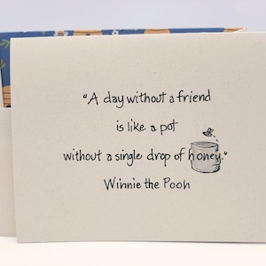 May include: A card with a quote from Winnie the Pooh: "A day without a friend is like a pot without a single drop of honey." The card is beige with black text and a small illustration of a honey pot and a bee.