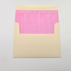 May include: A cream-colored envelope with a pink, textured flap.