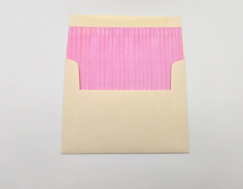 May include: A cream-colored envelope with a pink, textured flap.