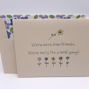 May include: A card with a floral design on the envelope and a message that reads "We're more than friends. We're really like a small gang!" with a small flower illustration above the text and five small flower illustrations below the text.