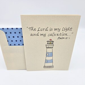 May include: A card with a lighthouse illustration and the text "The Lord is my light and my salvation..." Psalm 27:1. The card is beige with a blue and white polka dot envelope.