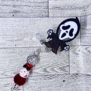 Può includere: Un portabadge a tema Halloween con un personaggio di Ghostface in bianco e nero. Il portabadge include un accento di perline con perline argentate, rosse e bianche e un pompon rosso scuro. Progettato per essere attaccato ai vestiti.