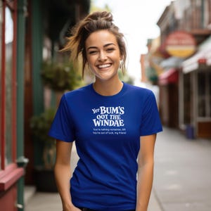 Peut inclure: Un t-shirt bleu roi à manches courtes avec le texte blanc Yer BUM'S OOT THE WINDAE, suivi du texte plus petit You're talking nonsense, OR You're out of luck, my friend, imprimé dans une police sans empattement sur la poitrine.