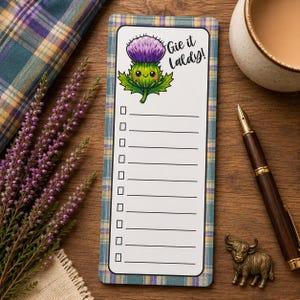 May include: A rectangular notepad with a blue and yellow plaid border featuring a cartoon purple thistle illustration and the text Gie it Laldy! at the top. The notepad includes ten horizontal lines with square checkboxes for list making.