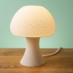 May include: A white mushroom-shaped table lamp with a textured, woven-like lampshade and a textured base. The lamp is on a wooden surface with a light green background. The lamp has a white cord.