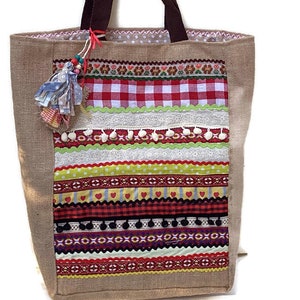 May include: A brown burlap tote bag with a colorful patchwork design. The design features red and white gingham, green and yellow stripes, and white pom-poms.