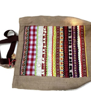 May include: A brown burlap tote bag with a colorful patchwork design. The patchwork is made of various ribbons, lace, and gingham fabrics in red, white, green, yellow, and black.