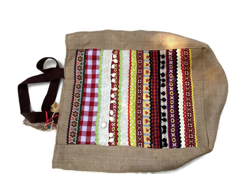 May include: A brown burlap tote bag with a colorful patchwork design. The patchwork is made of various ribbons, lace, and gingham fabrics in red, white, green, yellow, and black.