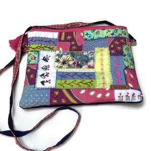 Puede incluir: Un bolso bandolera de estilo patchwork con un diseño de tela rosa, azul, verde y blanco. El bolso tiene una correa negra y una pequeña etiqueta de cuero marrón que dice "Handmade".