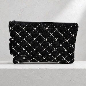 Könnte beinhalten: Eine schwarze, rechteckige Clutch mit einem gesteppten Rautenmuster aus weißen Nähten. An jeder Kreuzung des Rautenmusters ist eine kleine weiße Perle befestigt. Die Tasche verfügt über einen schwarzen Reißverschluss und einen schwarzen Quastenanhänger.