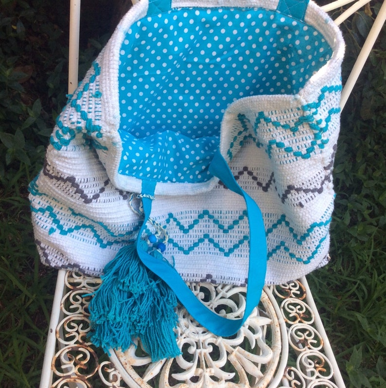Pode incluir: Sacola tote de croch&ecirc; branca com forro de bolinhas azuis e brancas. A sacola tem um tassel azul e uma al&ccedil;a de fita azul.