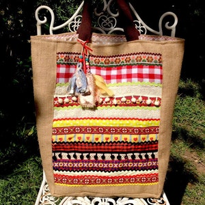 May include: A large, brown burlap tote bag with a colorful patchwork design. The bag is decorated with red and white gingham, yellow, red, and green ribbons, and white lace. The bag has a brown handle and a tassel.