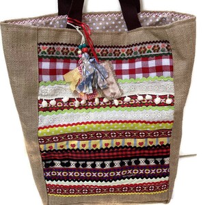 May include: A large, brown burlap tote bag with a patchwork design. The bag features a variety of colorful fabrics, including red and white gingham, yellow and green stripes, and floral patterns. The bag has brown fabric handles and a tassel charm.