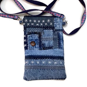 Może przedstawiać: Mała denimowa torebka na ramię z patchworkowym wzorem. Torebka jest wykonana z różnych odcieni niebieskiego denimu i ma białe szwy oraz zapięcie na guzik. Torebka ma długi regulowany pasek.