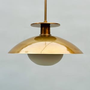 May include: A mid-century modern pendant light fixture with a brass finish. The light has a rounded, bowl-shaped shade and a frosted glass globe at the bottom. The fixture is suspended from a brass rod.