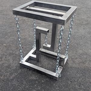 May include: A metal sculpture featuring an impossible shape, appearing to defy gravity. The structure is made of square metal tubing and suspended by chains. The sculpture is a unique piece of art.